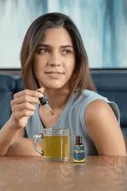 Smiling woman holding a dropper of KeySlim Drops above a cup of tea, suggesting ease of use and satisfaction with the product